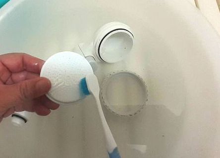 分解したシャワーヘッドを古い歯ブラシでこする様子