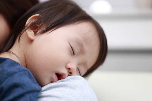 親の肩で眠る子ども